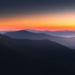 Mountains are silhouetted against a vibrant sunrise.